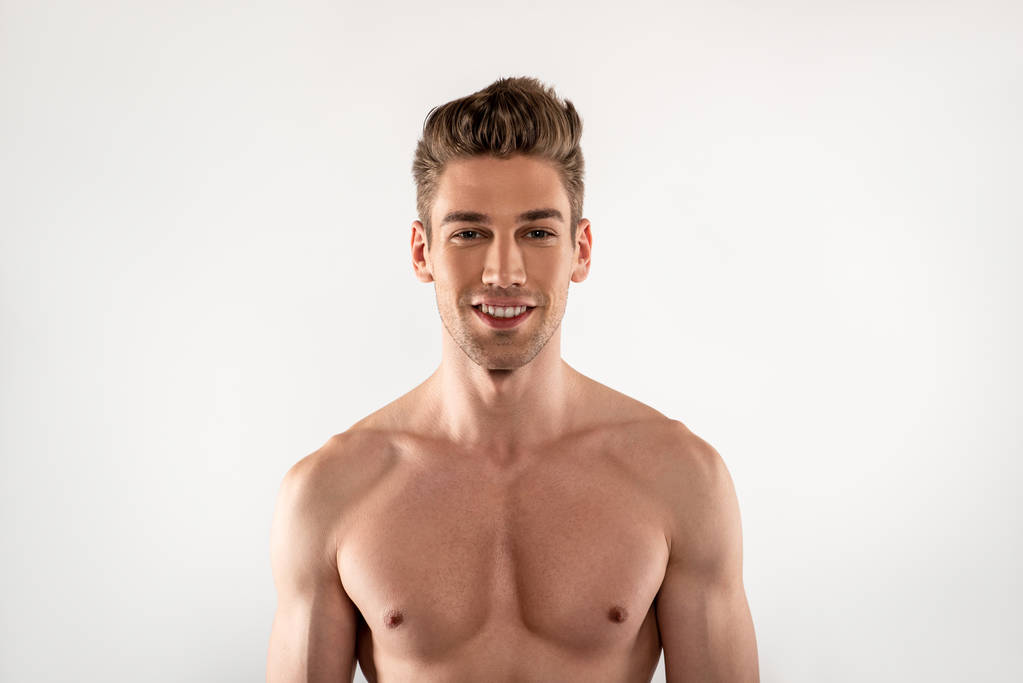 Aantrekkelijke jonge man met perfecte lichaam staande tegen witte achtergrond - Foto, afbeelding