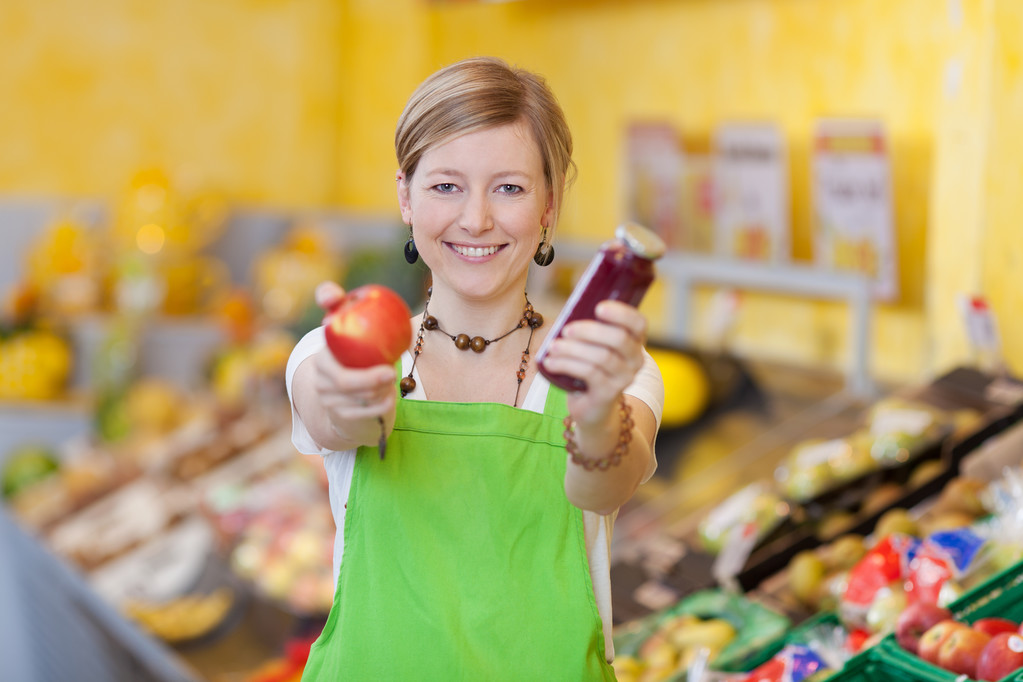 Trabajadora sosteniendo tarro de manzana y mermelada en tienda de comestibles
 - Foto, Imagen