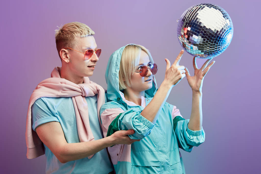 Jeune couple de danseurs à la mode posant avec boule disco sur fond violet
 - Photo, image