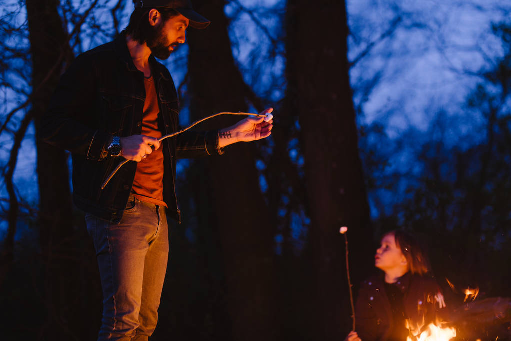 Felice padre sta di fronte a un fuoco nella foresta tenendo rametti in mano la notte
. - Foto, immagini