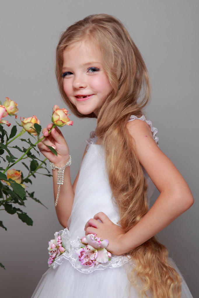 Menina caucasiana com belos cabelos longos saudáveis segurando rosas amarelas com folhas verdes em um fundo cinza
 - Foto, Imagem