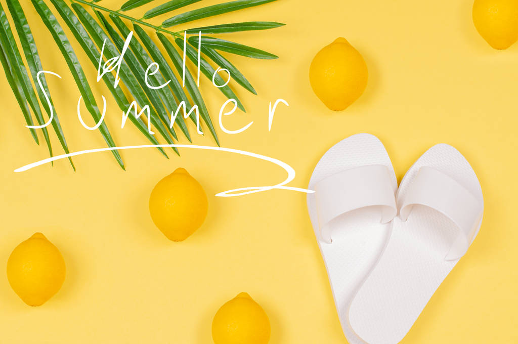 Hello Summer text on yellow background with lemon, sandals and green tropical palm leaf. - Photo, Image