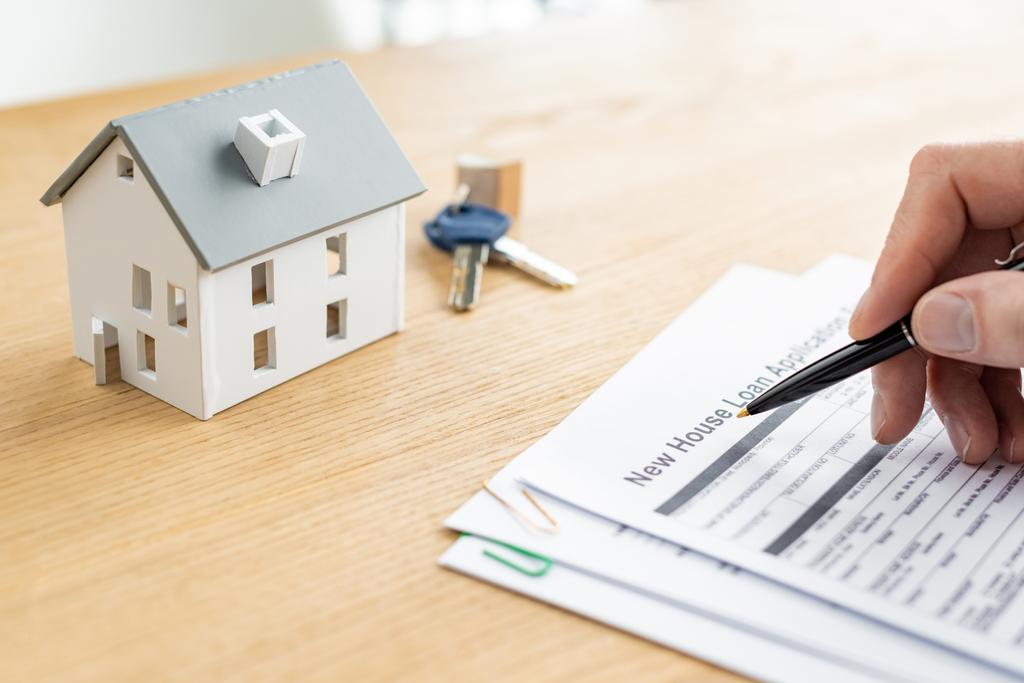 cropped view of house dealer holding pen near document with new house loan lettering, house model and keys  - Photo, Image