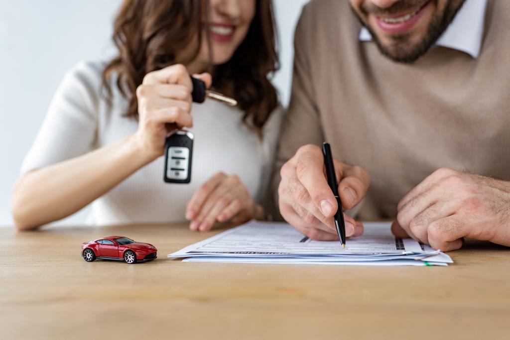 あごひげの男署名契約と車のキーを保持している女性の近くに赤いおもちゃの車の選択的な焦点  - 写真・画像