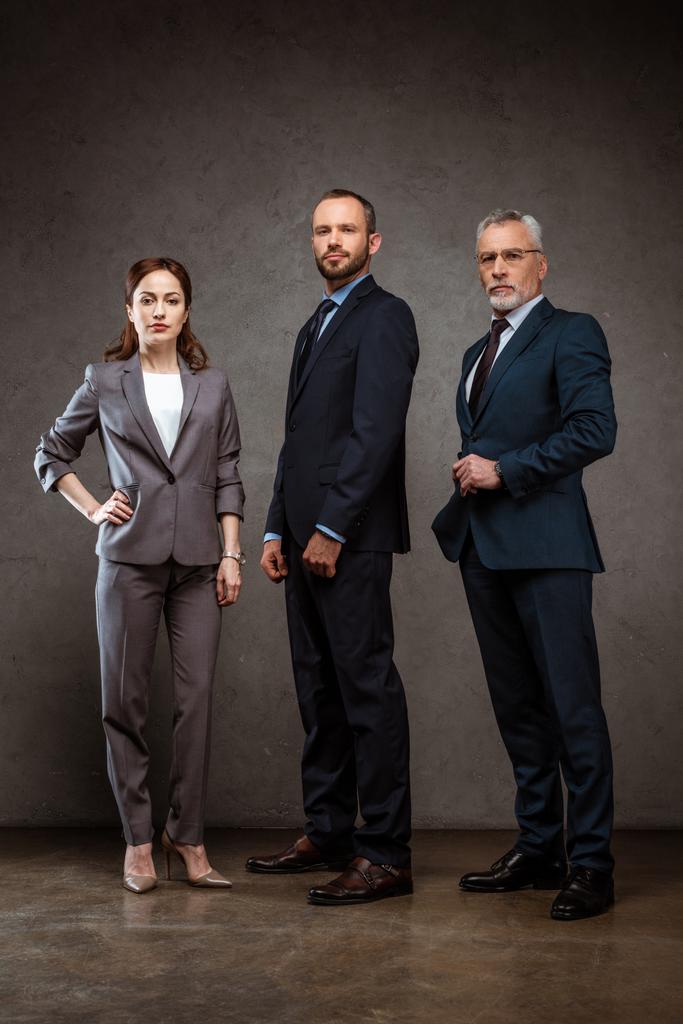 Tiefansicht einer Geschäftsfrau, die mit der Hand auf der Hüfte neben gutaussehenden Geschäftsleuten auf grau steht - Foto, Bild