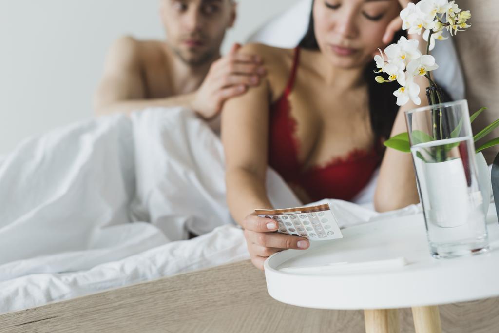enfoque selectivo del hombre tocando hombro de novia asiática sosteniendo píldoras anticonceptivas
 - Foto, Imagen