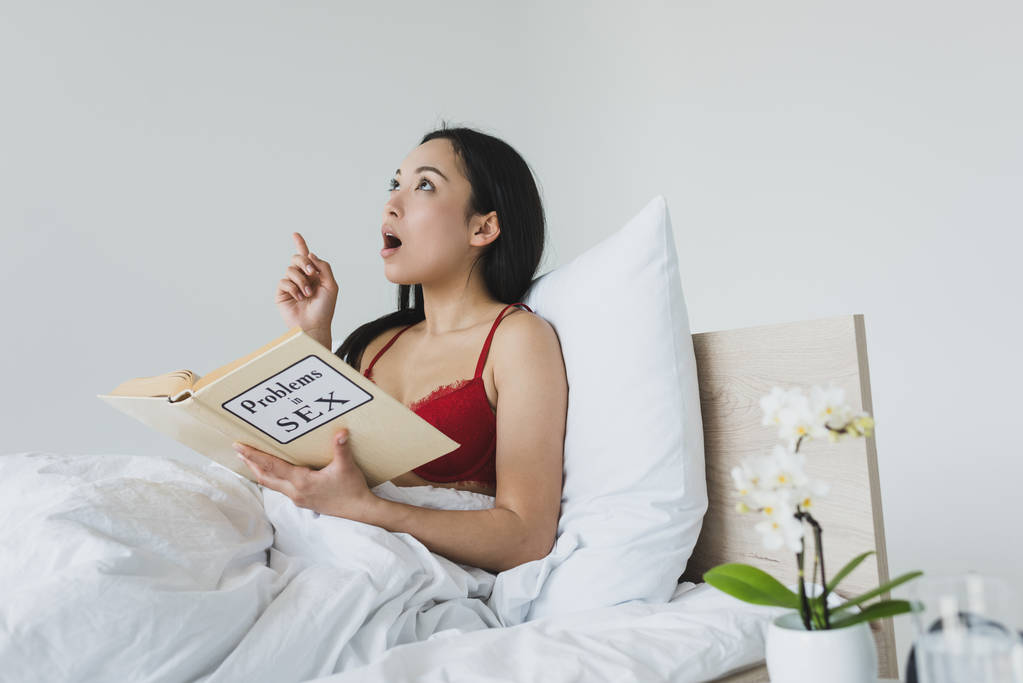 surprised asian woman showing idea sign while reading problems in sex book  - Photo, Image
