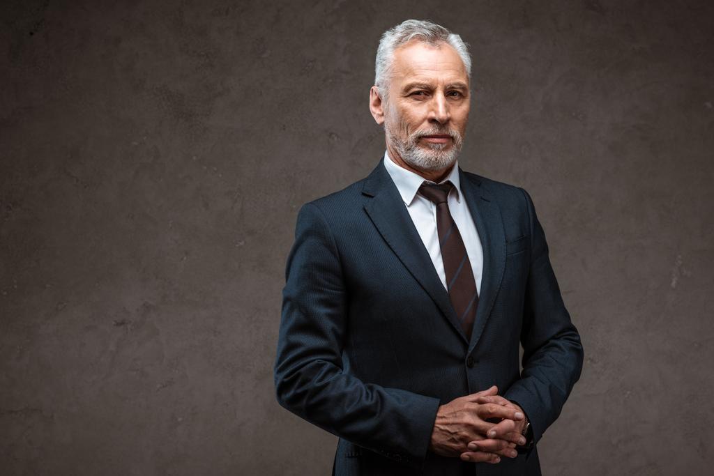 успешный бизнесмен в костюме, стоящий с сжатыми руками на сером
  - Фото, изображение