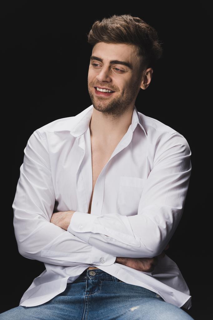 χαρούμενος όμορφος άντρας με λευκό πουκάμισο χαμογελά και κοιτάζοντας μακριά απομονωμένη σε μαύρο - Φωτογραφία, εικόνα