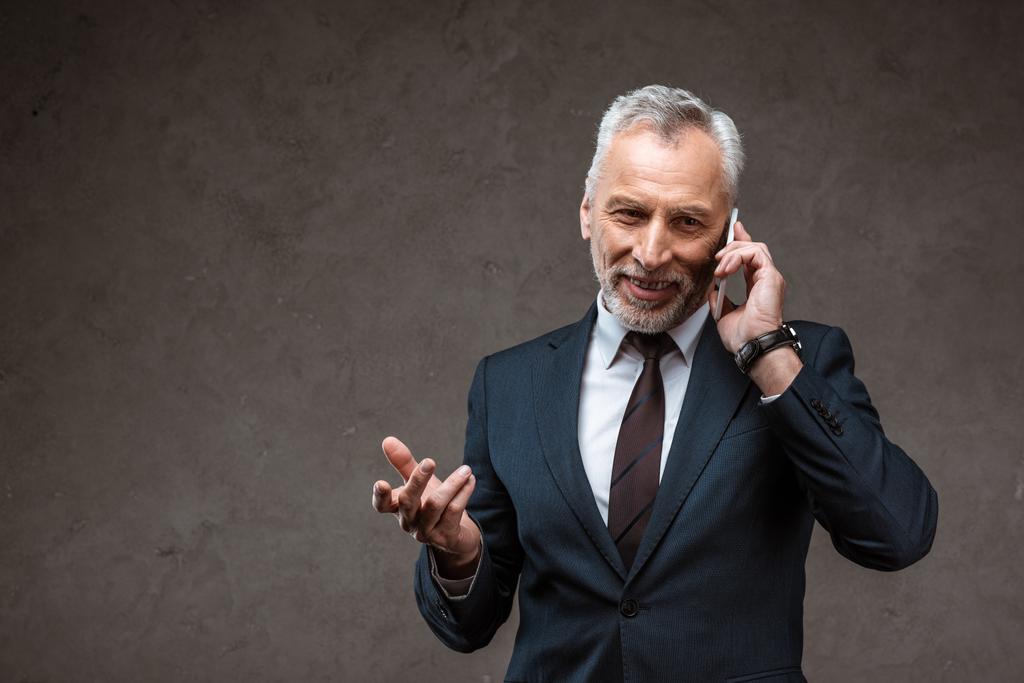 веселый бизнесмен в костюме разговаривает на смартфоне и жестикулирует на сером
  - Фото, изображение