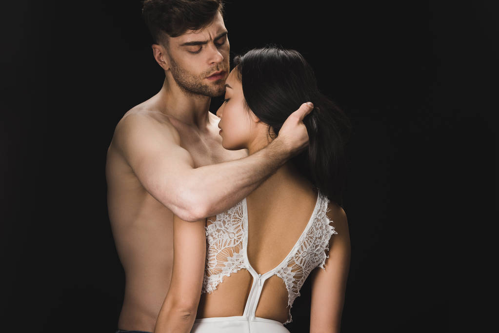 knappe shirtless man knuffelen sexy vriendin in witte lingerie geïsoleerd op zwart - Foto, afbeelding