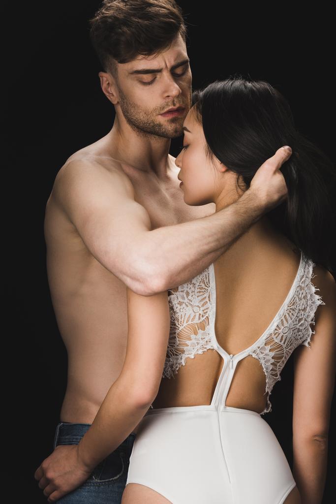 jong shirtless man knuffelen sexy vriendin in wit lingerie geïsoleerd op zwart - Foto, afbeelding