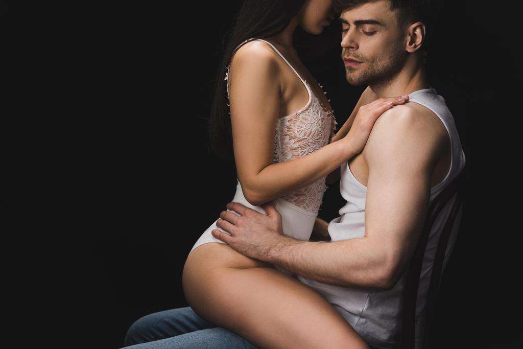 vue partielle de la femme en lingerie blanche assise sur les genoux d'un bel homme isolé sur noir
 - Photo, image