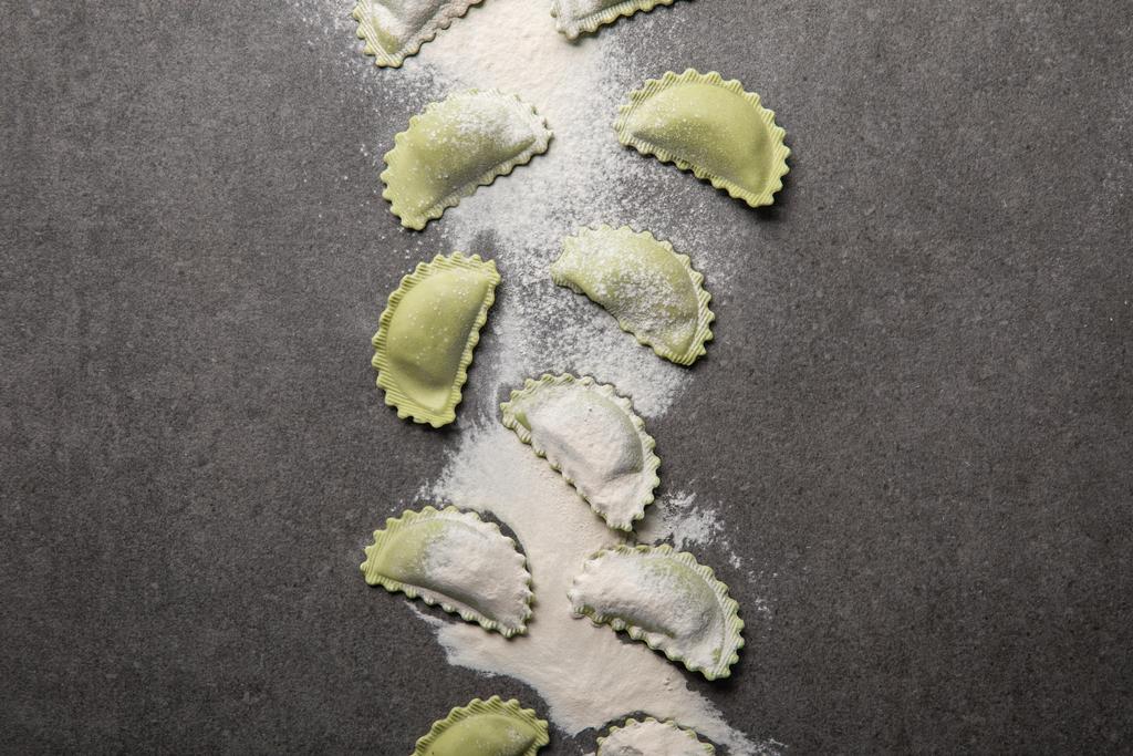 Widok z góry na surowe zielone ravioli z rozproszonym mąką na szarej powierzchni teksturowanej - Zdjęcie, obraz