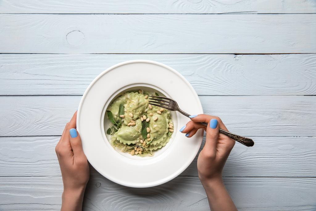 bijgesneden uitzicht van vrouw eten groene ravioli met pijnboompitten en salie op houten tafel - Foto, afbeelding