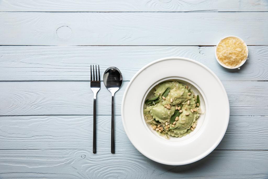 vista superior de ravioles verdes con piñones y salvia servida con queso rallado en mesa de madera
  - Foto, imagen