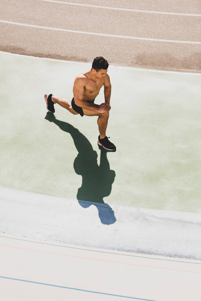 mixed race shirtless sportsman in sneakers stretching at stadium - Photo, Image