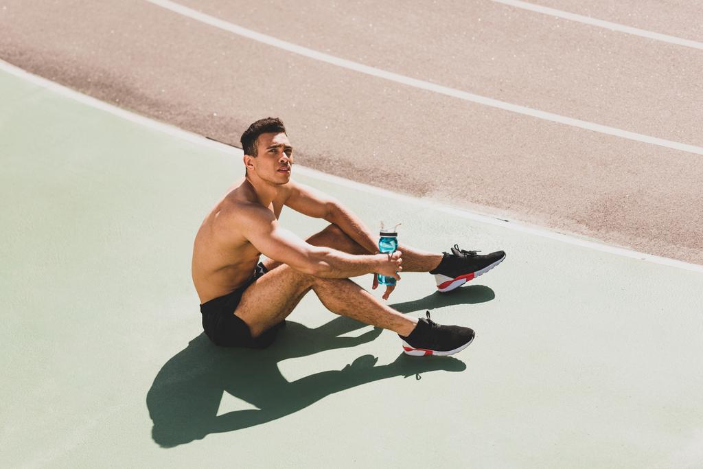 stadyumda oturan yorgun yakışıklı karışık yarış sporcusu - Fotoğraf, Görsel