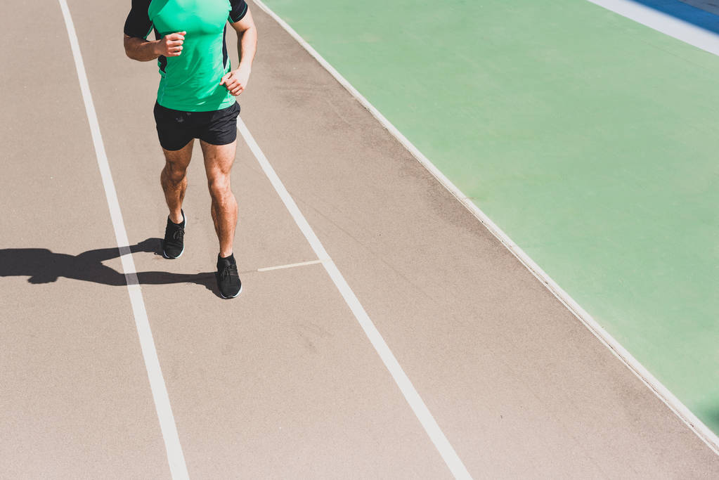 wykadrowany widok sportowca w odzieży sportowej biegną na stadionie - Zdjęcie, obraz