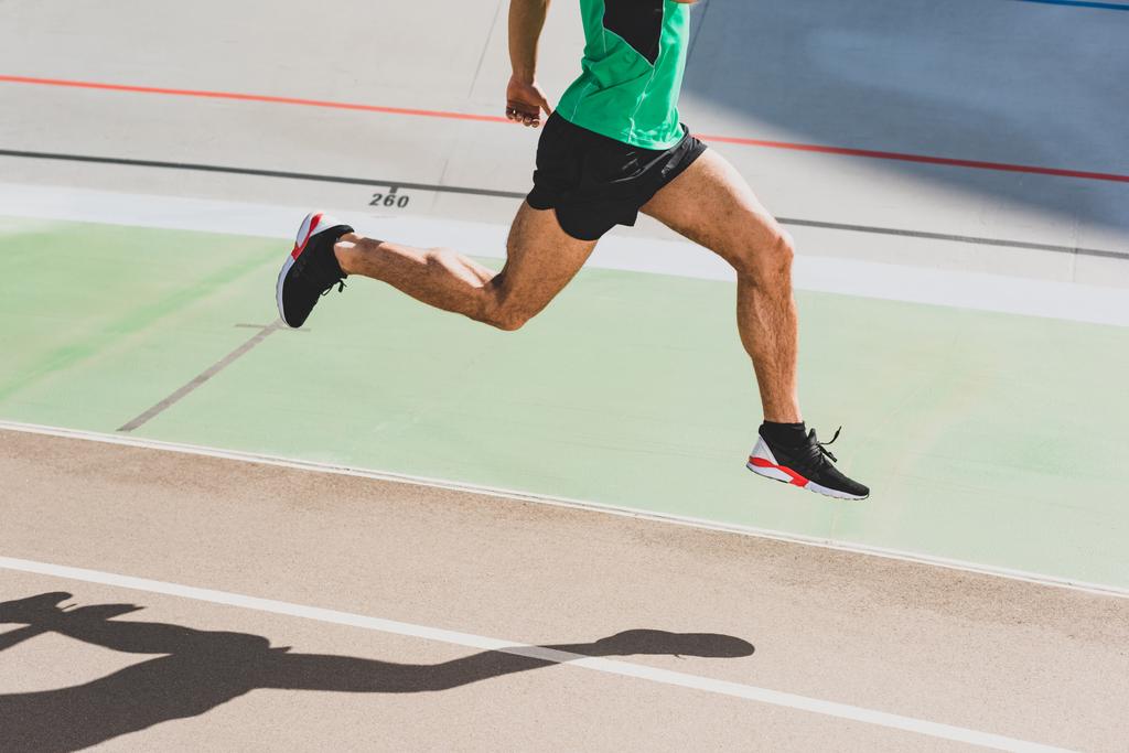 περικομμένη θέα του αθλητή σε μαύρα αθλητικά παπούτσια που τρέχουν στο στάδιο - Φωτογραφία, εικόνα