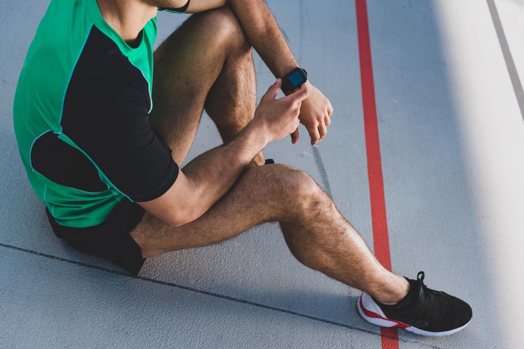 cropped view of mixed race sportsman using smartwatch at running track  - Photo, Image