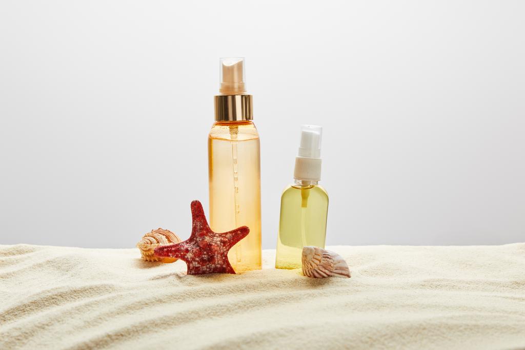 gri arka planda deniz kabukları ve denizyıldızı ile kum şeffaf şişelerde güneşten için ürünler - Fotoğraf, Görsel