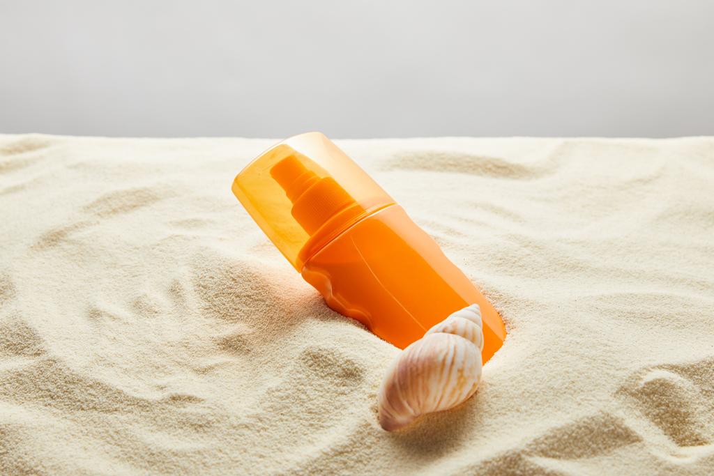 сонцезахисний крем в помаранчевій пляшці в піску з черепашкою на сірому фоні
 - Фото, зображення