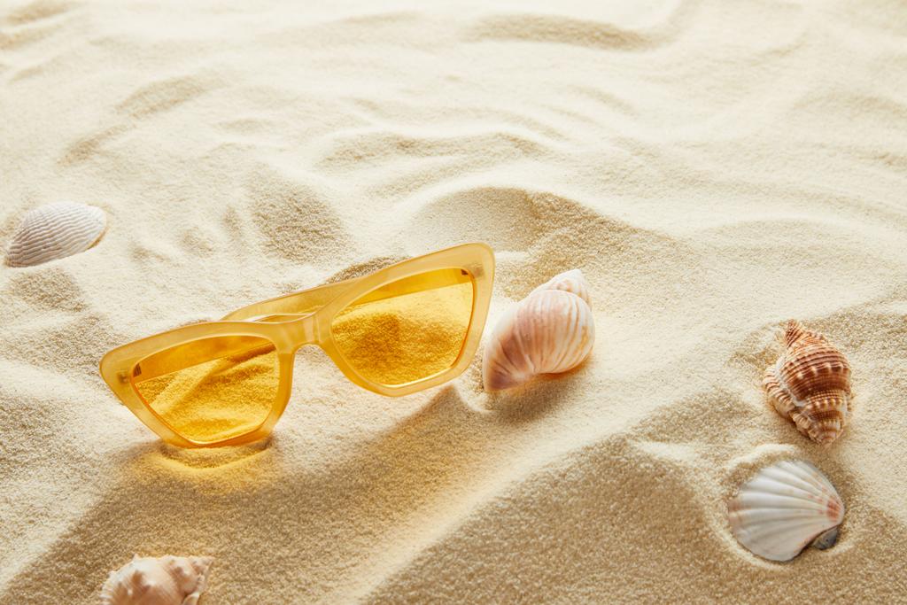 sárga stílusos napszemüveg homokon kagylókkal - Fotó, kép