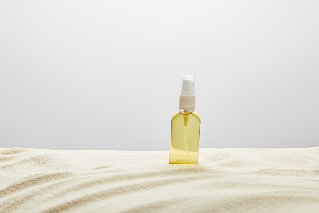 aceite bronceador en botella transparente de spray amarillo en arena sobre fondo gris
 - Foto, imagen