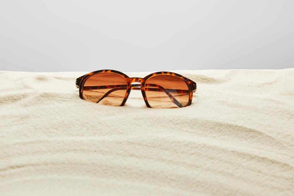 brown stylish sunglasses on sand on grey background - Photo, Image