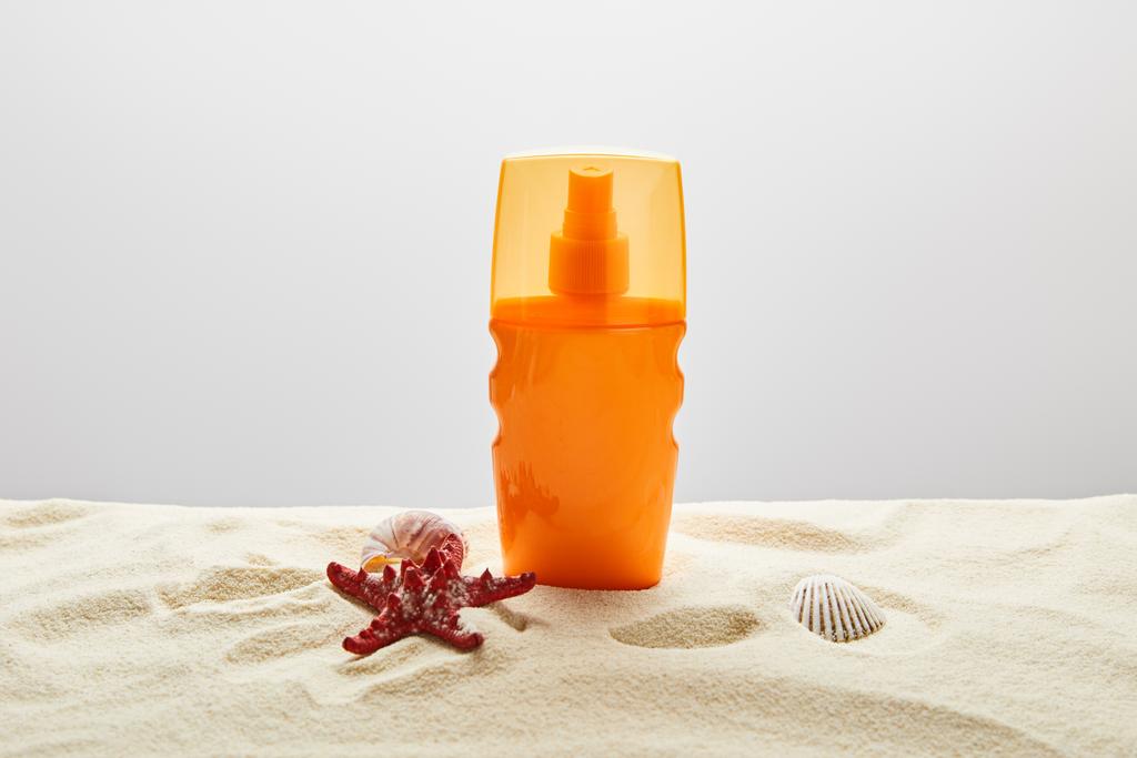 krém na opalování v oranžovém lahvích s červenými hvězdými rybami a mušle na písku na šedém pozadí - Fotografie, Obrázek