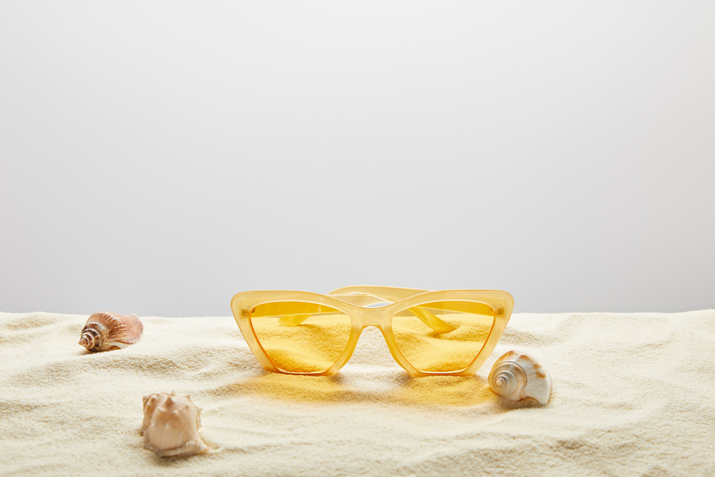 gele stijlvolle zonnebril op zand met schelpen op grijze achtergrond - Foto, afbeelding