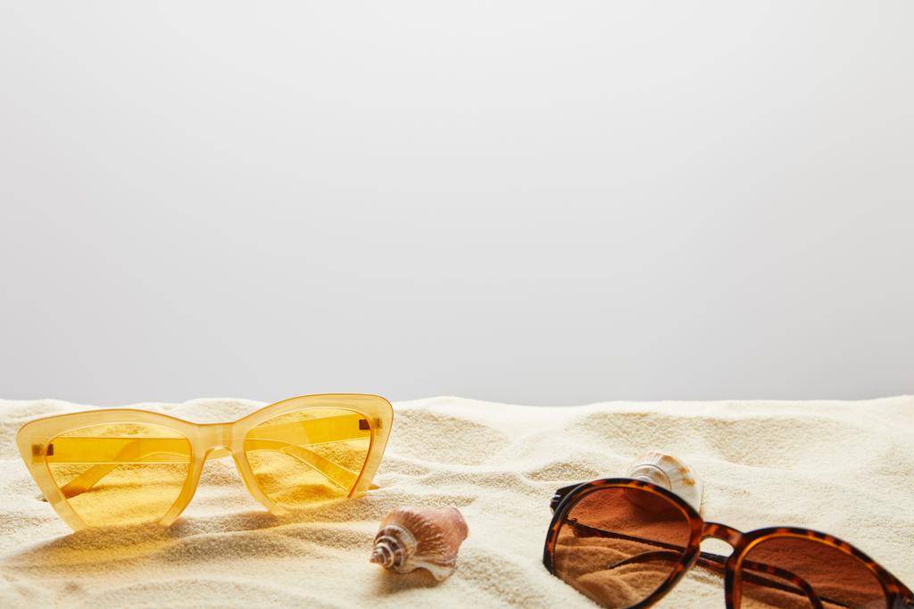 желтые и коричневые стильные солнцезащитные очки на песке с ракушками на сером фоне
 - Фото, изображение