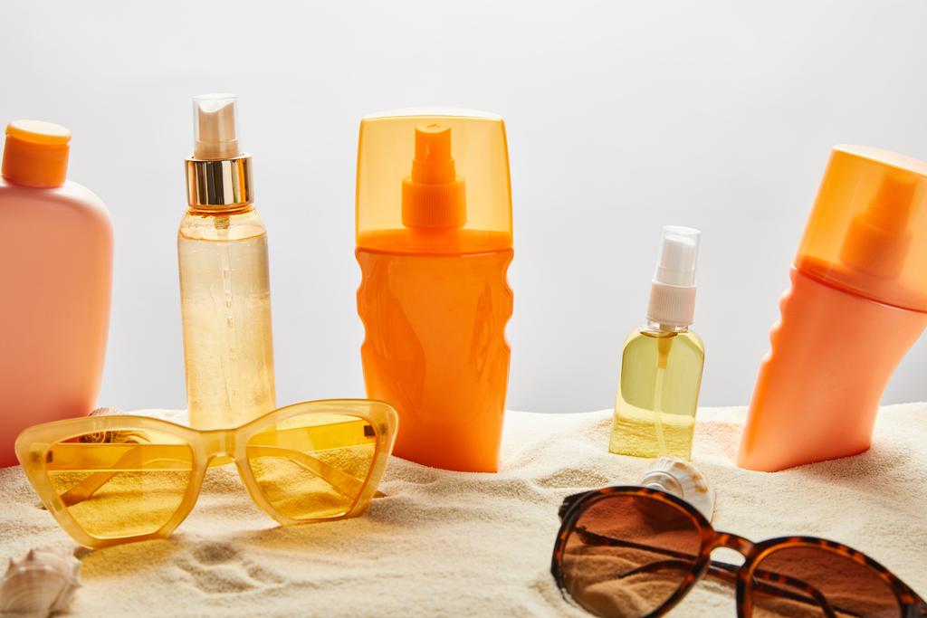 various sunscreen products in bottles on sand near fashionable sunglasses and seashells on grey background - Photo, Image