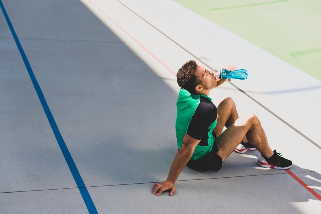 sportovní sportovec sedící na běžícím a pitnou vodu z modré láhve  - Fotografie, Obrázek