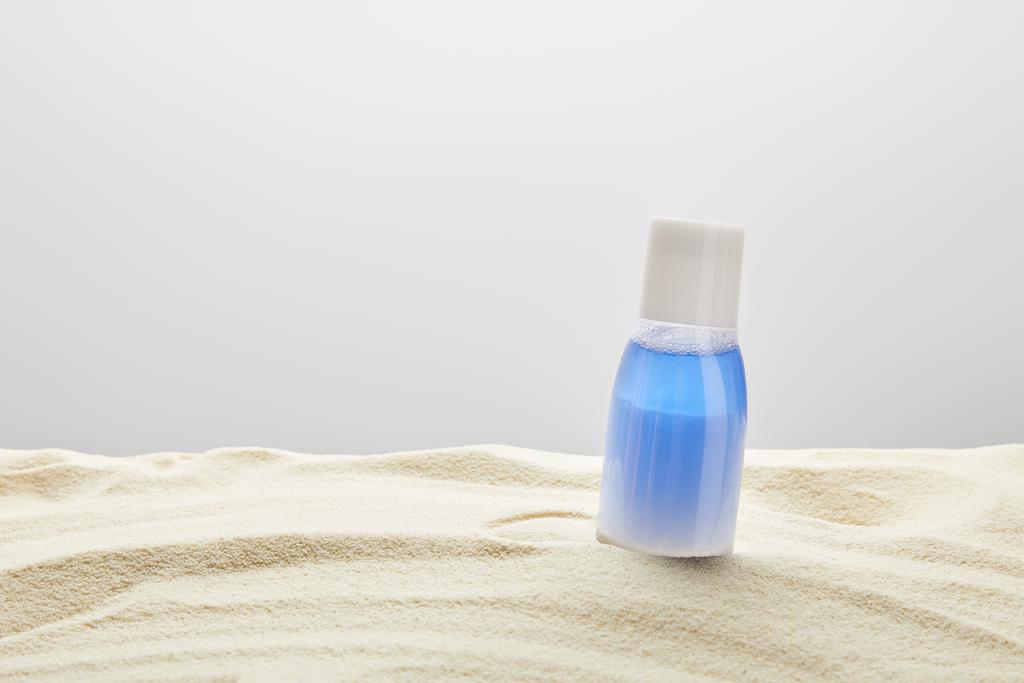 filtr przeciwsłoneczny niebieski balsam w butelce w piasku na szarym tle z kopią przestrzeni - Zdjęcie, obraz