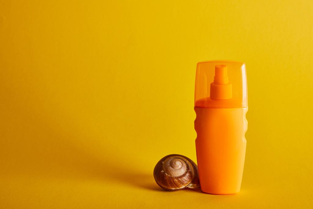 zonnebrandcrème in oranje fles in de buurt van Seashell op donker gele achtergrond - Foto, afbeelding