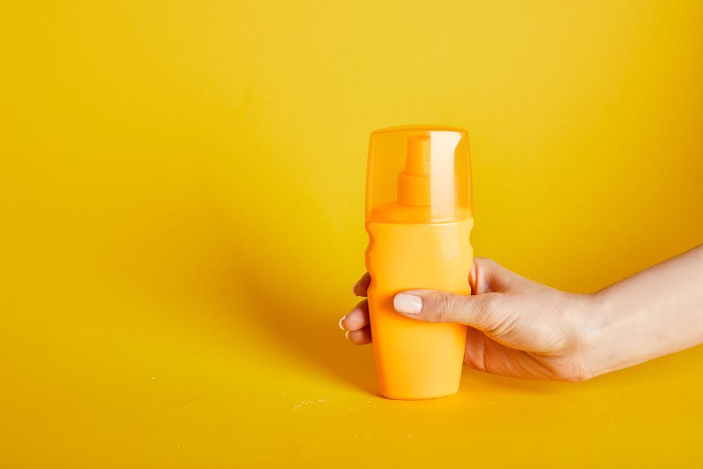 bijgesneden beeld van de vrouw houden zonnebrandcrème in fles op gele achtergrond - Foto, afbeelding