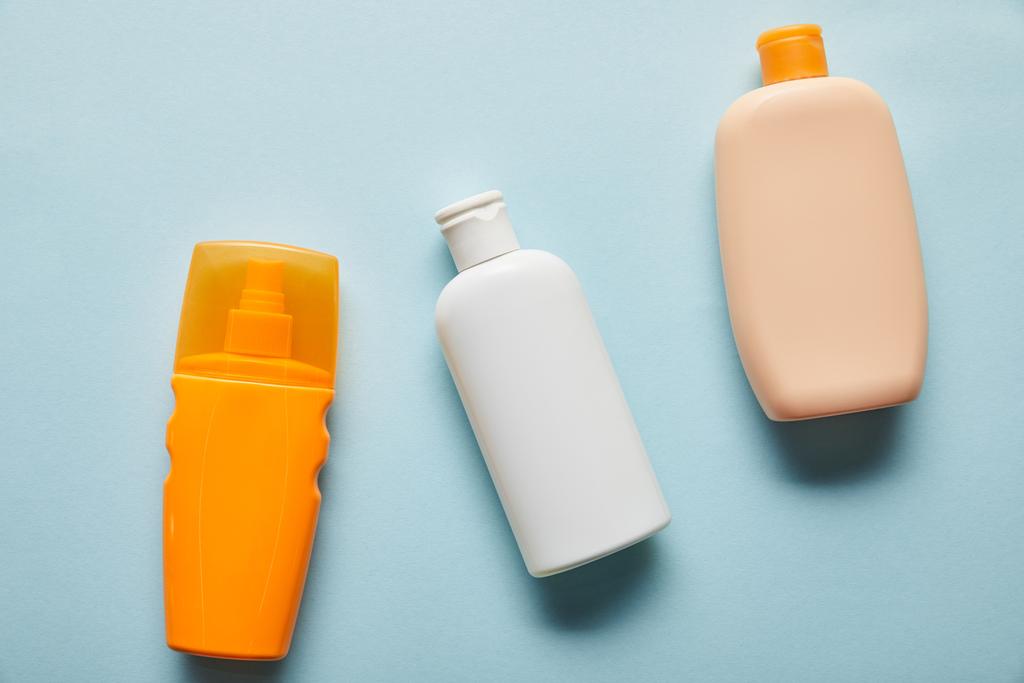 Top zicht op zonnebrandcrème producten in flessen op blauwe achtergrond - Foto, afbeelding