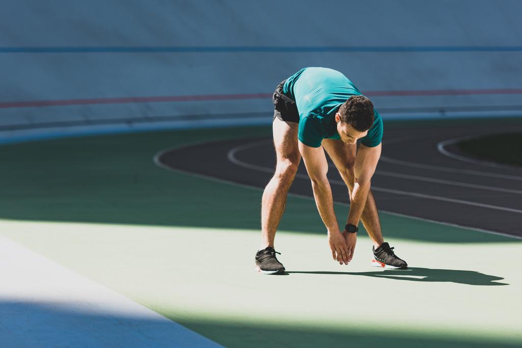 deportista de carrera mixta estirándose en el estadio, de pie a la luz del sol en el suelo verde
  - Foto, imagen