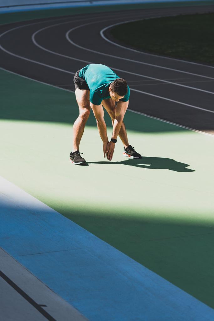 desportista de raça mista aquecendo no estádio, de pé no chão verde à luz do sol
 - Foto, Imagem