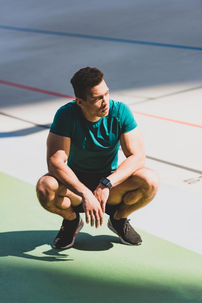 muscular mixed race sportsman squatting at stadium in sunlight - Photo, Image