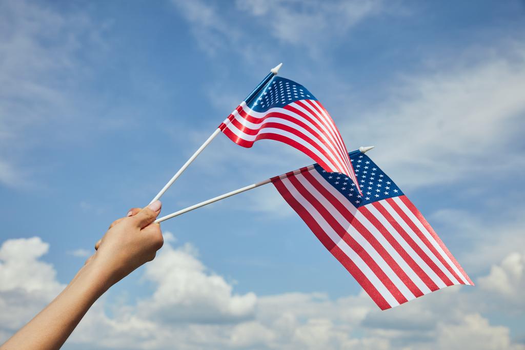 Ausgeschnittene Ansicht einer Frau mit amerikanischen Flaggen in der Hand auf blauem Himmelshintergrund - Foto, Bild