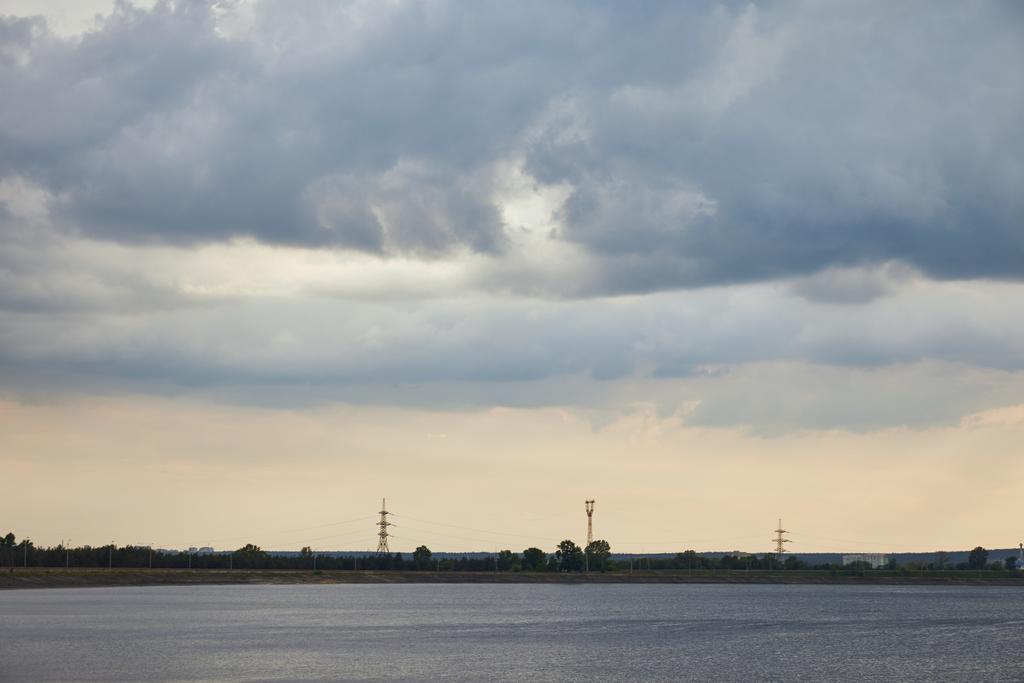 Blauwe wolken, rivier en kust met elektrische palen op zonsondergang achtergrond - Foto, afbeelding