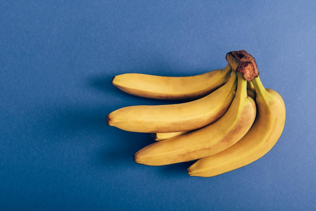 Vista superior de racimo maduro de plátanos deliciosos sobre fondo azul
 - Foto, imagen