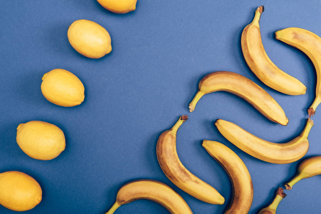 Вид зверху на жовті лимони та свіжі банани на синьому фоні
 - Фото, зображення