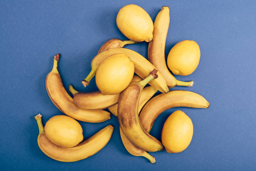 Vista superior de bananas maduras e amarelas e limões sobre fundo azul
 - Foto, Imagem