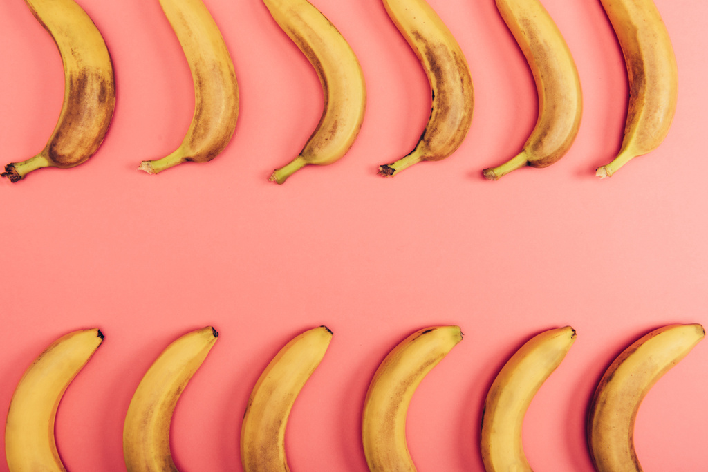 コピースペースを持つサンゴの背景に熟した黄色のバナナのトップビュー - 写真・画像