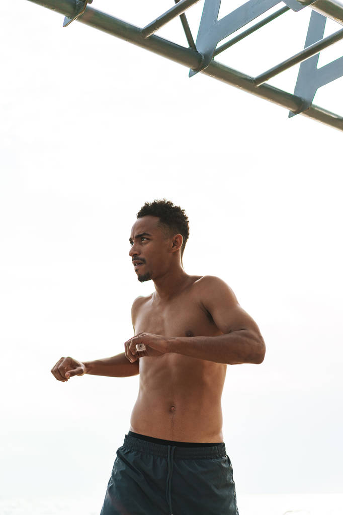 Bello giovane uomo sportivo africano all'aperto in spiaggia mare a piedi fare esercizi
. - Foto, immagini