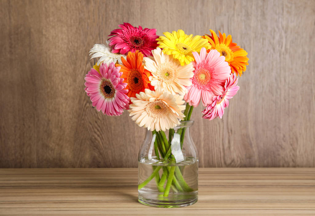 Bouquet of beautiful bright gerbera flowers in glass vase on table against wooden background - Photo, Image